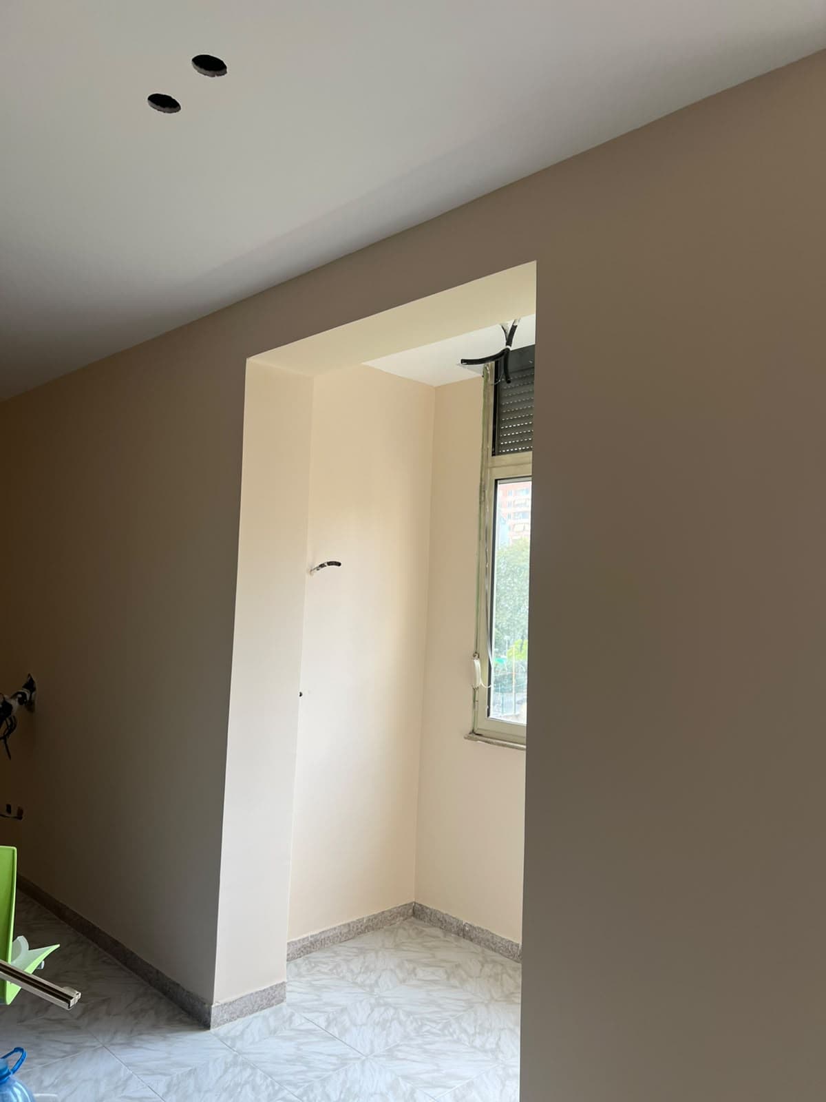 Dhomë e rikonstruktuar me mure të lyera dhe hapje gipsi drejt dritares