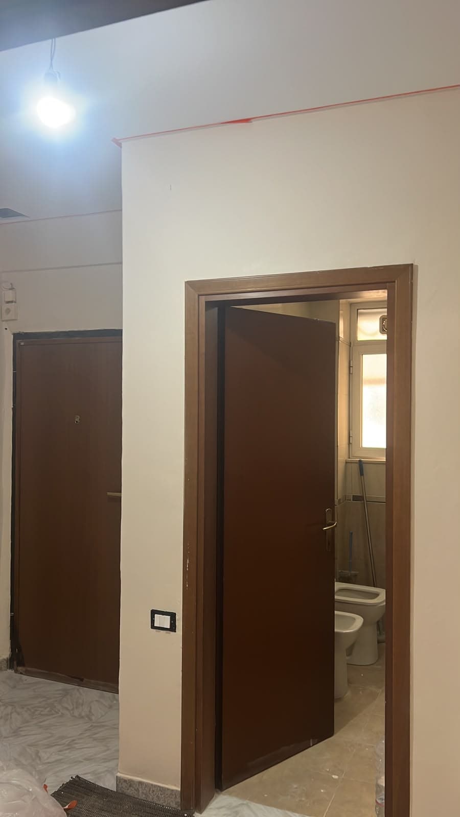 Hyrje me mure të lyera, dyer druri dhe ndriçim në tavan